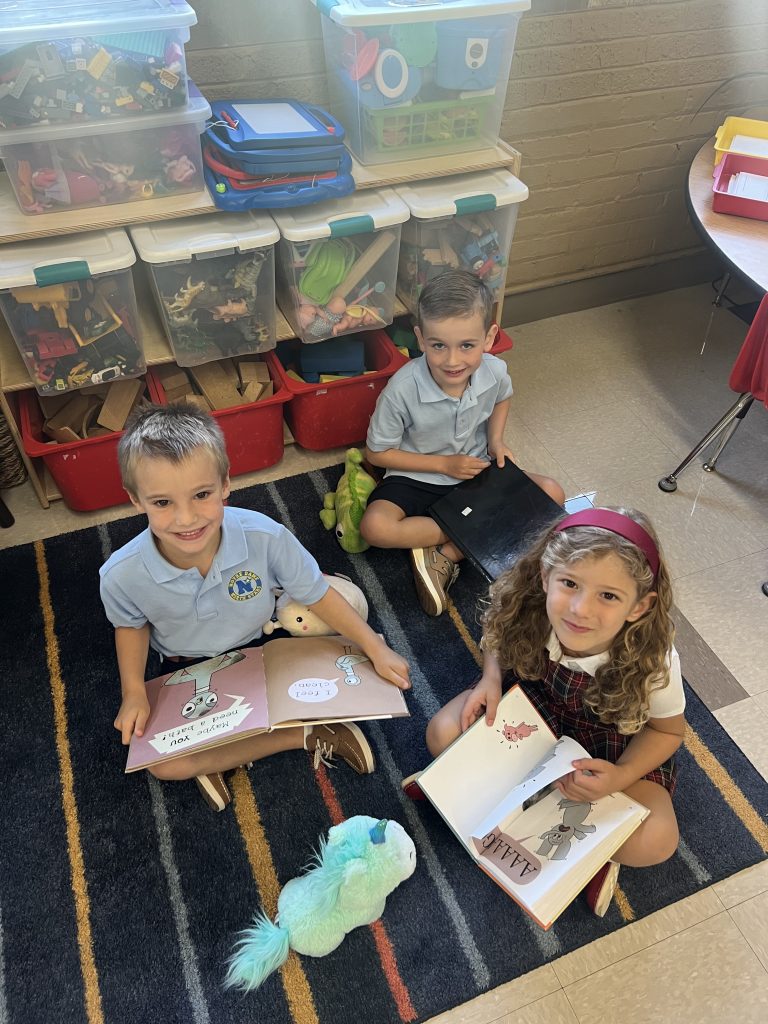 3 kindergarten students reading on carpet. 