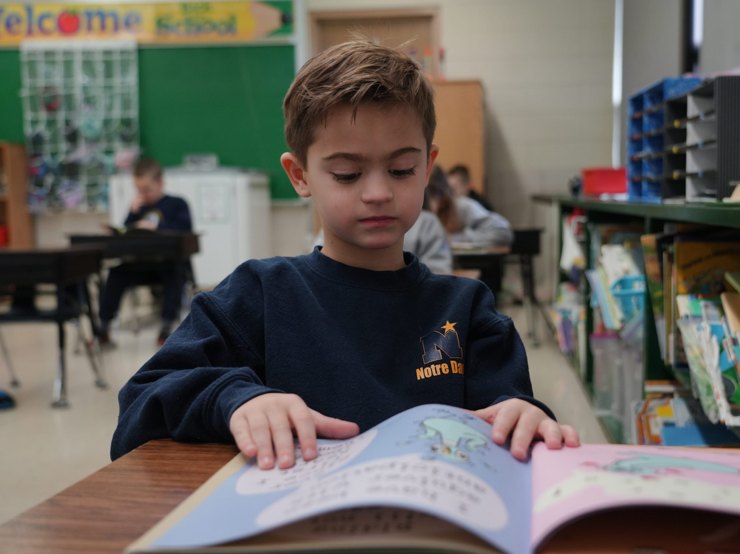 1st grade student reading a book at their desk.