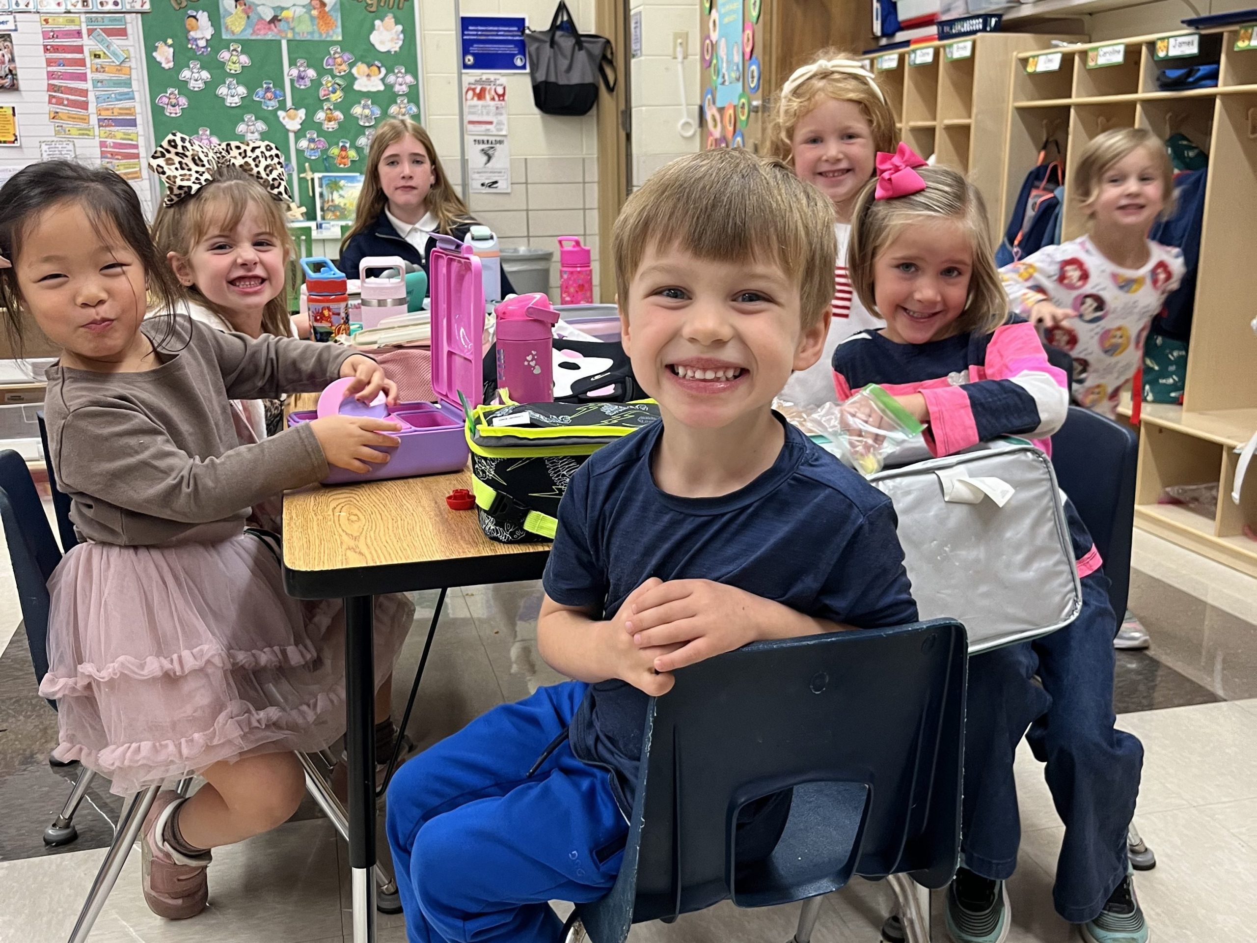 Preschool students eating lunch at a table with their 7th grade lunch monitor.