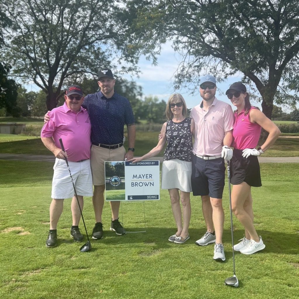 Family poses for photo as it plays the Mayer Brown-sponsored hole at the 2024 John Janicik Open